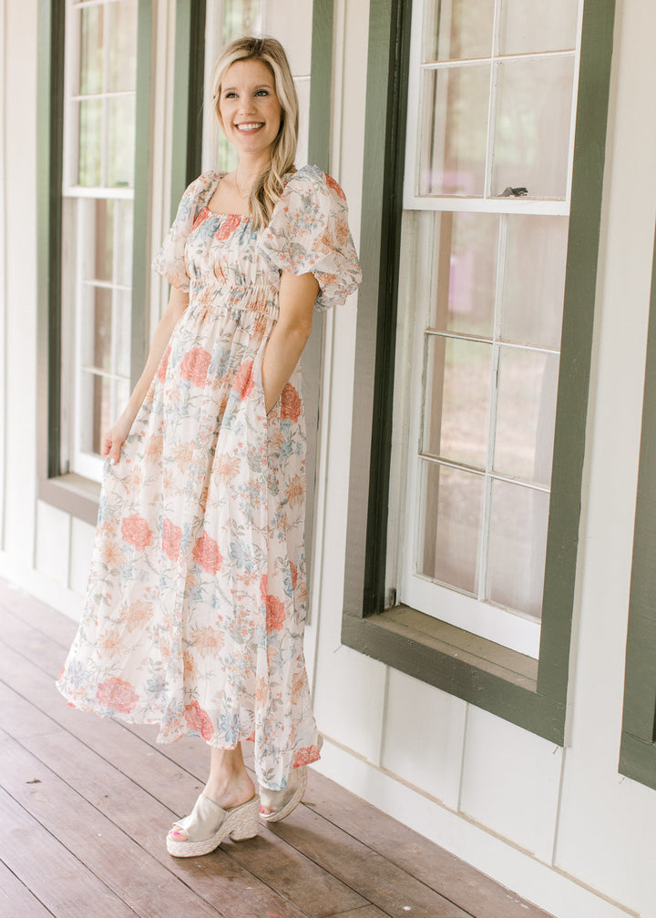 Model wearing wedges with a cream dress with pink, blue and yellow floral and bubble short sleeves.