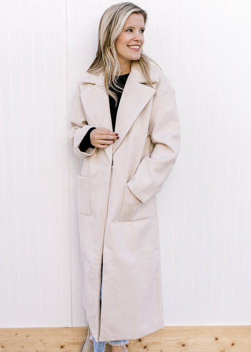 Model wearing a cream long line jacket with front pouch pockets, collar and a snap closure.  