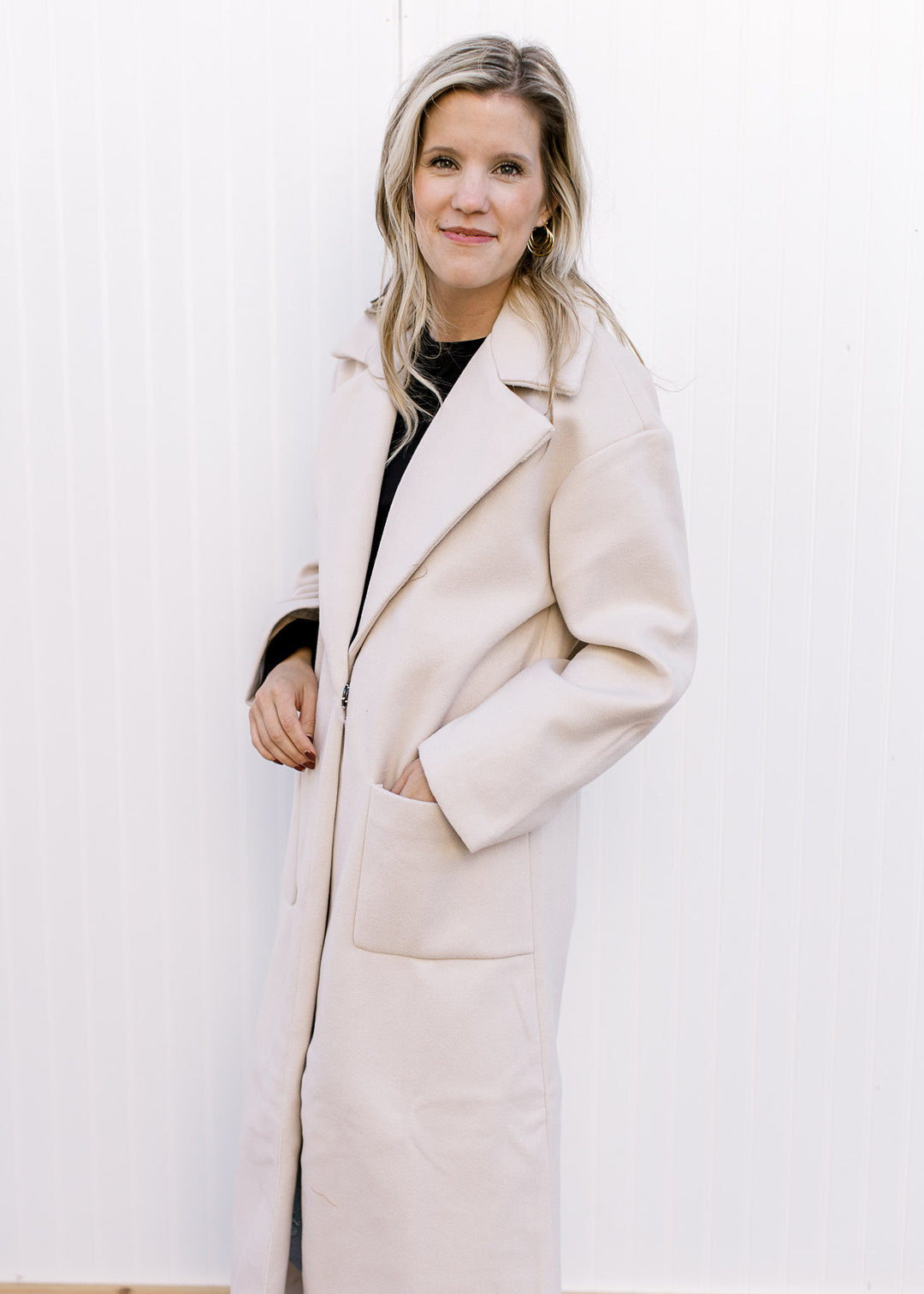 Model wearing a cream long line jacket with front pouch pockets, collar and a long sleeves. 