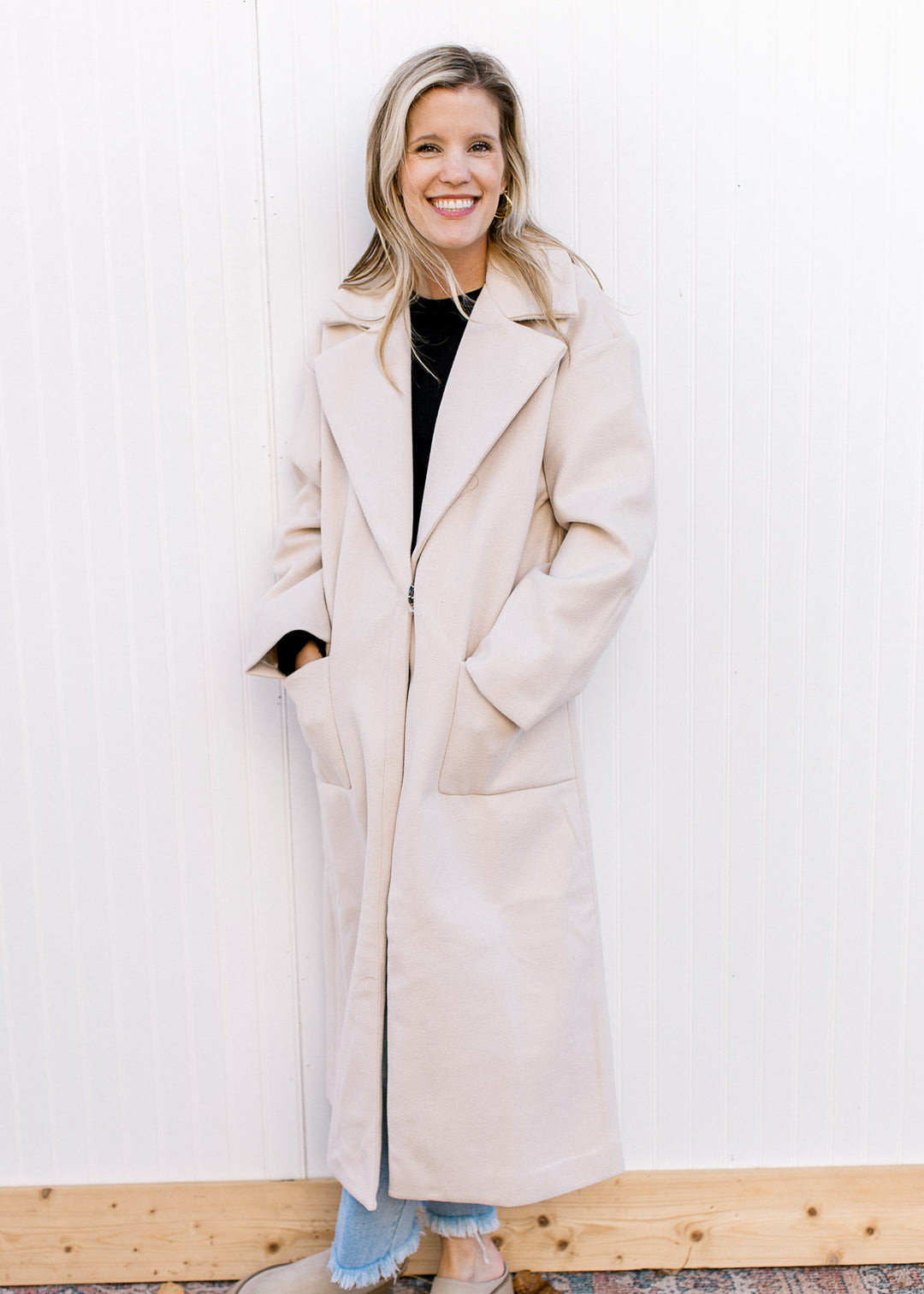 Model wearing jeans and a cream long line jacket with front pouch pockets and a collar. 