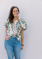 Model wearing jeans and a cream top with olive print, bubble short sleeves and button closure. 