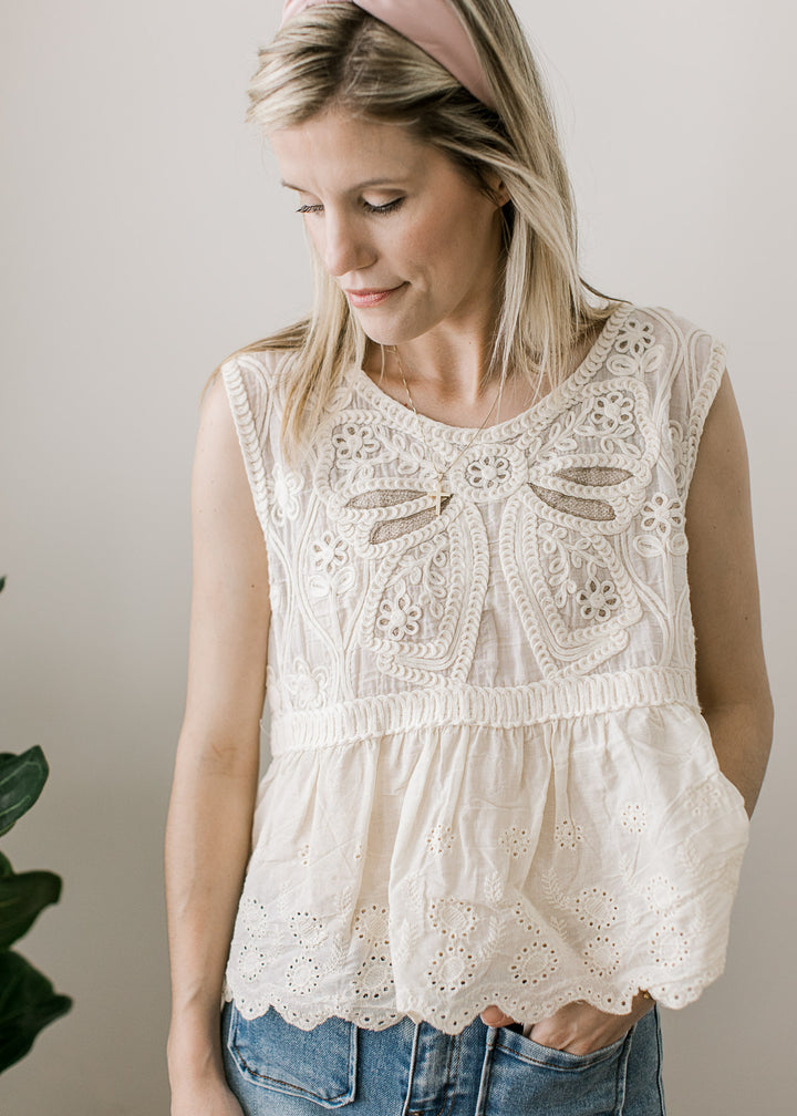 Model wearing a cream sleeveless top with crochet floral, open knit back and scalloped hem.