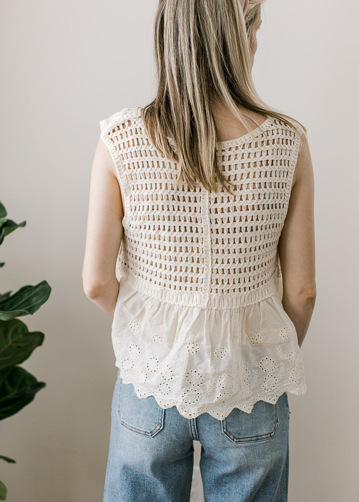 Back view of model in a cream sleeveless top with crochet floral, open knit back and scalloped hem.