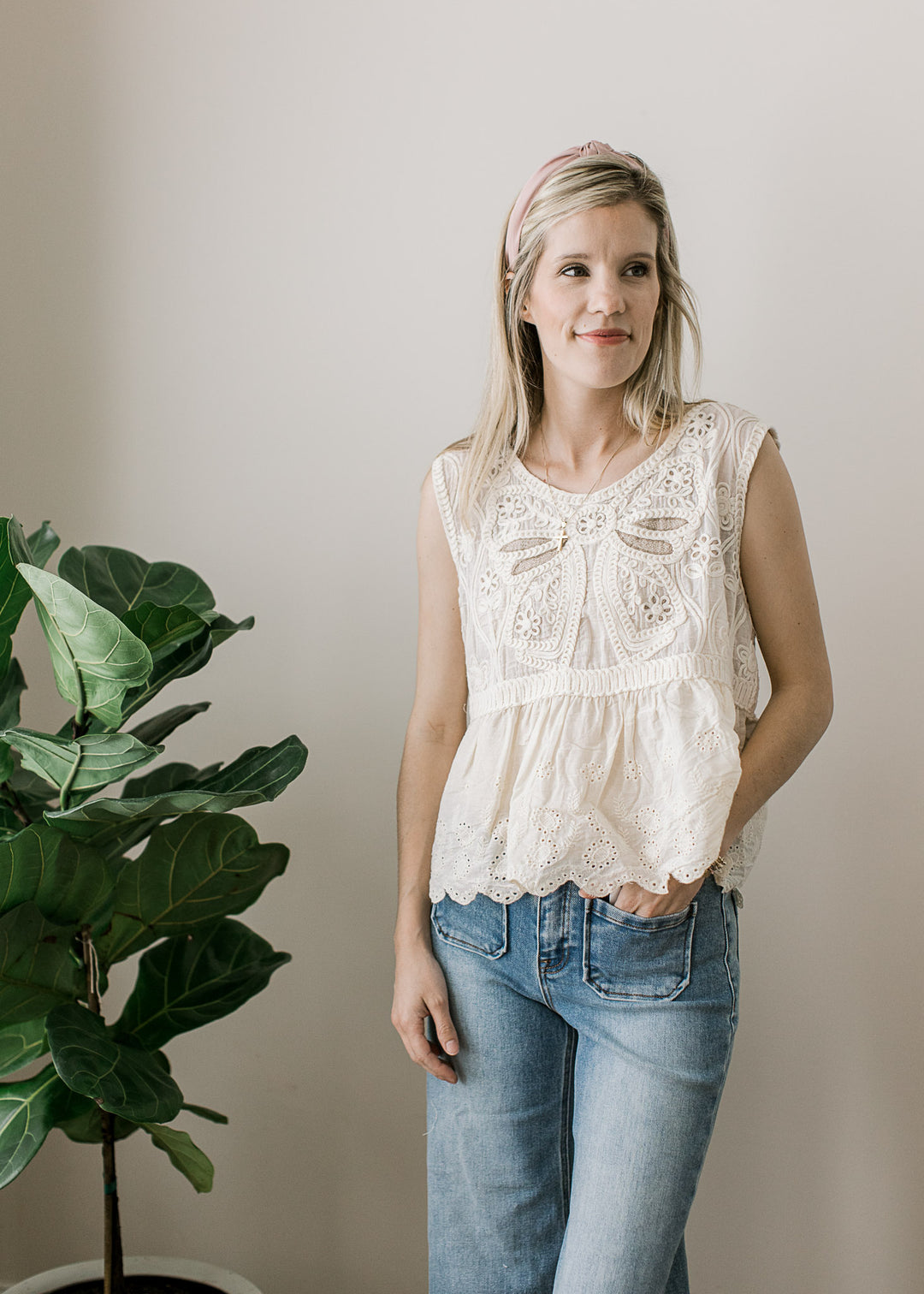 Model wearing jeans and a cream top with crochet floral, open knit back and scalloped hem.