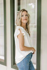 Side view of ruffle cap sleeve on a white top with a ruffle v-neck and placket