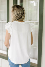 Back view of white top with ruffle cap sleeve and ruffle at neck and placket.