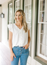 Model wearing jean with a white top with ruffle cap sleeves, ruffle at v-neck and down placket. 