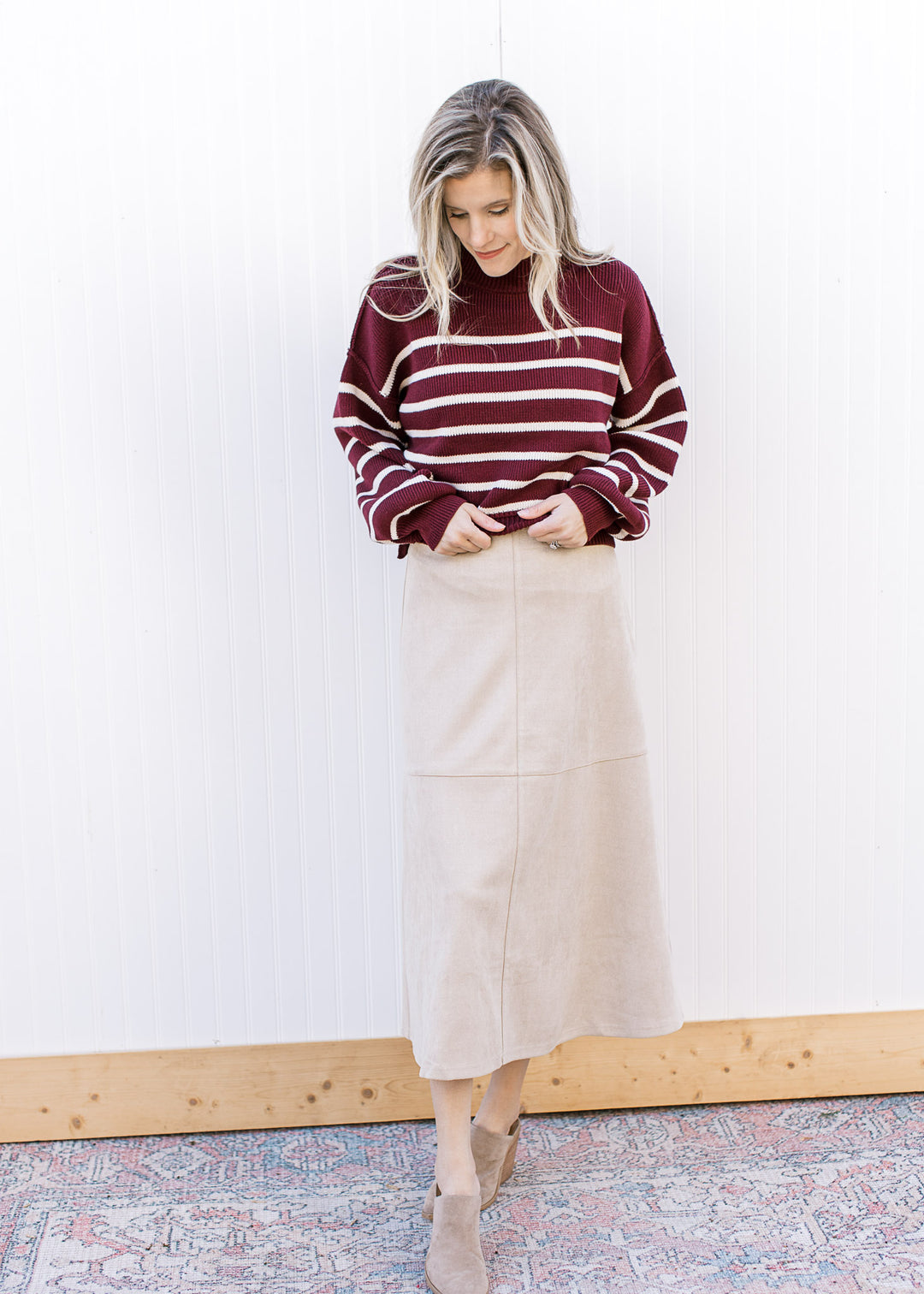 Model wearing a burgundy sweater, booties and a cream suede midi with a hidden side zipper.