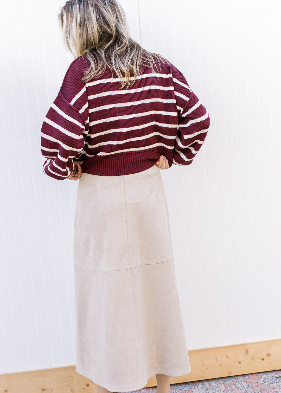 Back view of Model wearing a burgundy sweater and a cream suede midi with a hidden side zipper. 