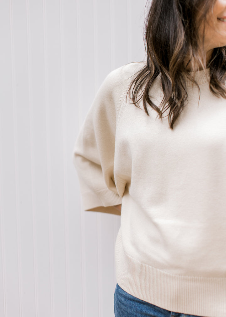 Close up of round neck and 3/4 sleeve on a cream sweater with ribbing at neck, hem and sleeves. 