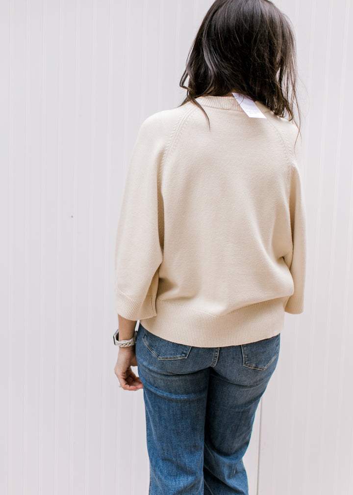Back view of Model wearing a cream sweater with a round neck, 3/4 sleeve and lightweight material. 