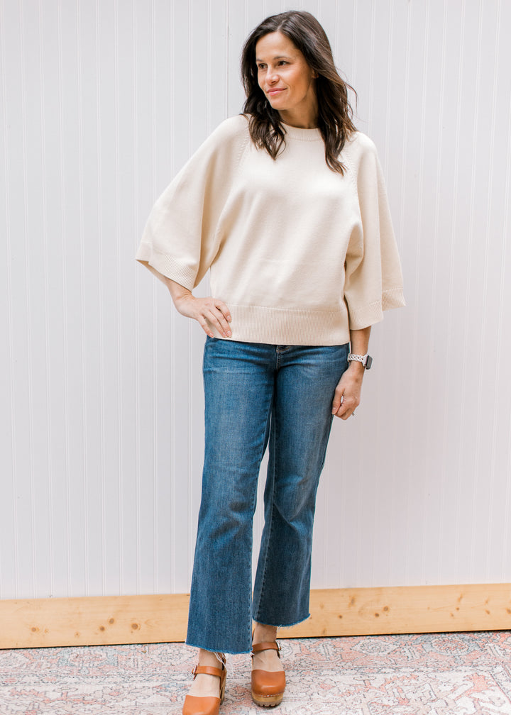 Model wearing a cream sweater with a round neckline, 3/4 sleeve and lightweight material. 
