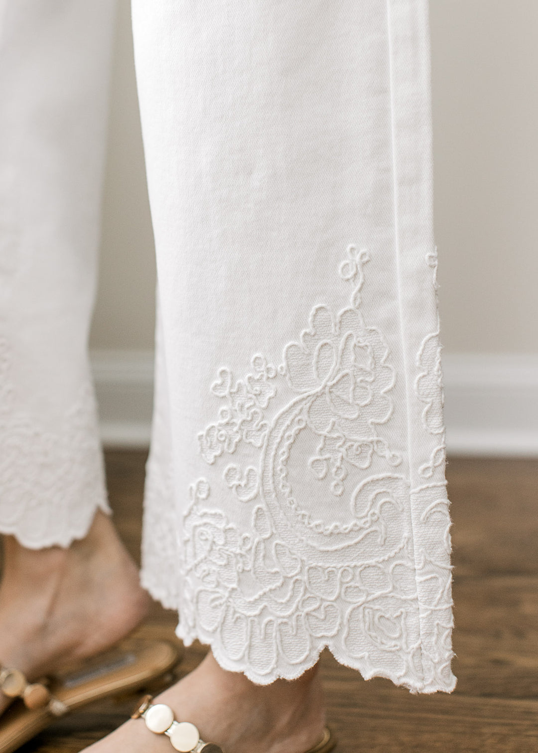Close up of tone-on-tone embroidery at hemline of creamy white wide leg pants with tummy control.