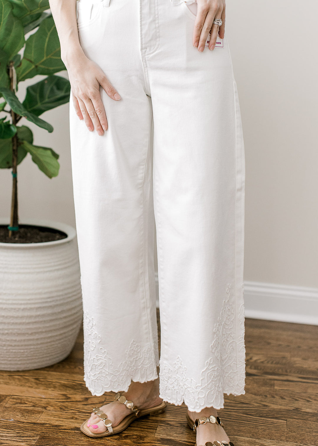 Model wearing sandals and white wide-leg cropped jeans with tone-on-tone embroidery at hem.