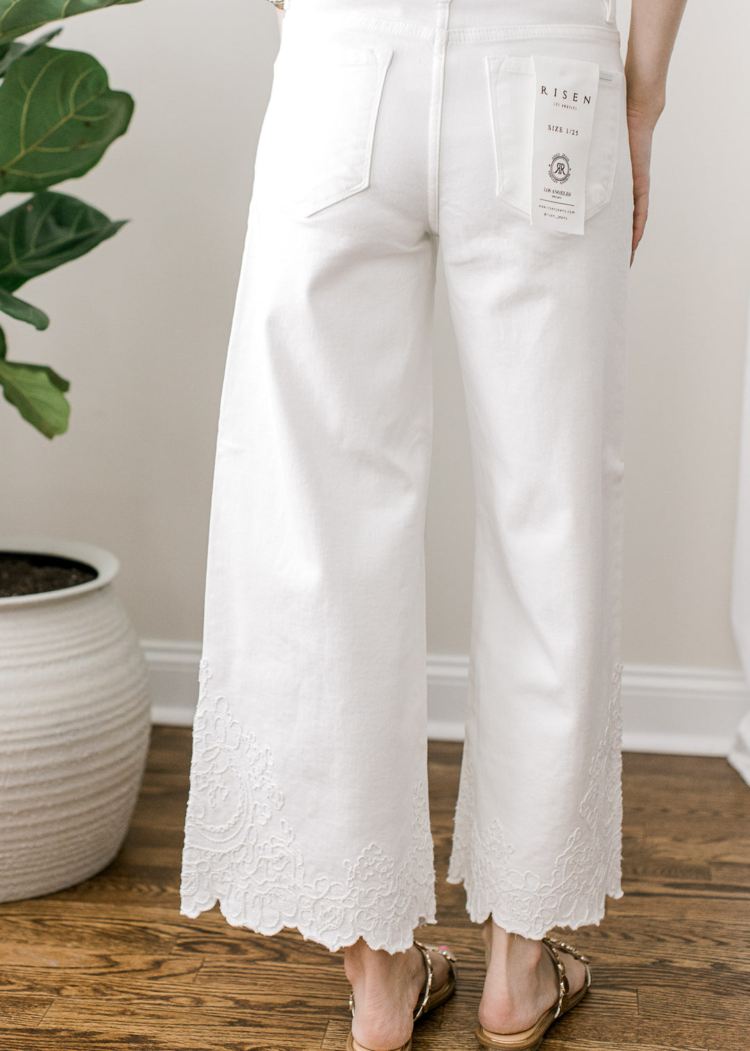 Back view of Model wearing a white wide-leg cropped jeans with tone-on-tone embroidery at hem.
