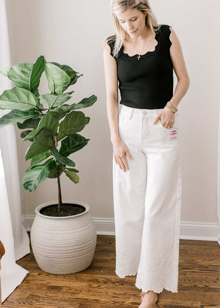 Model wearing a black top and white wide-leg cropped jeans with embroidered hemline. 