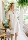 Model wearing a cream denim dress with contrast stitching ,v-neck, patch pockets and short sleeves.
