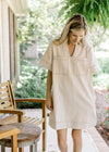 Model wearing a cream above the knee dress with contrast stitching ,v-neck and short sleeves.