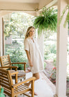 Model wearing sandals with a cream denim dress with a v-neck, patch pockets and short sleeves.