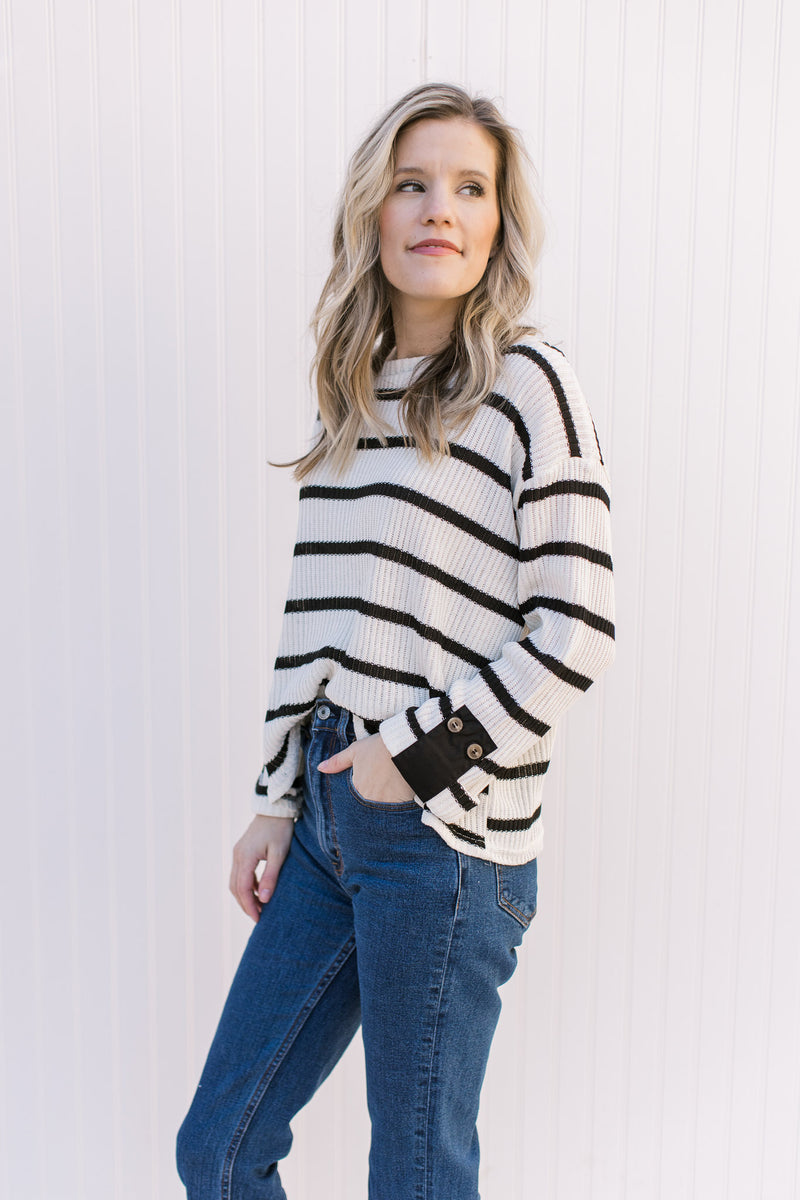 Side view of Model wearing a cream sweater with black stripes and contrasting placket at cuff. 