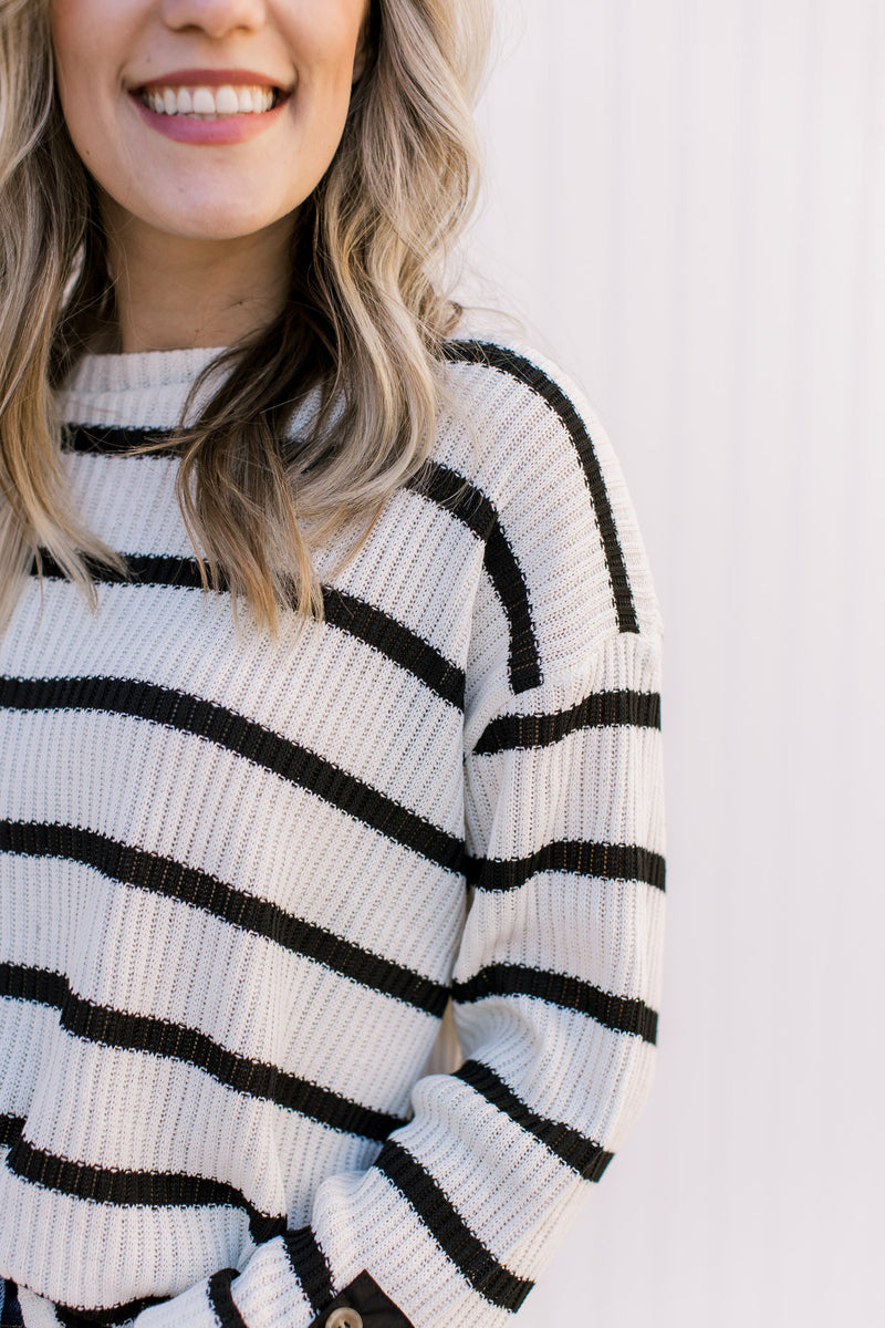 Close up of ribbing and round neck on a cream sweater with  black stripes and long sleeves. 