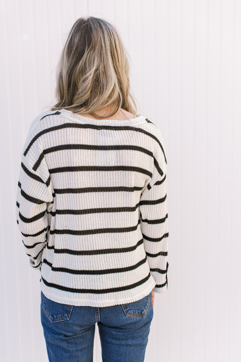 Back view of Model wearing a ribbed cream sweater with black stripes and a round neck.
