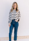 Model wearing jeans and a cream sweater with black stripes and contrasting placket at cuffed sleeve