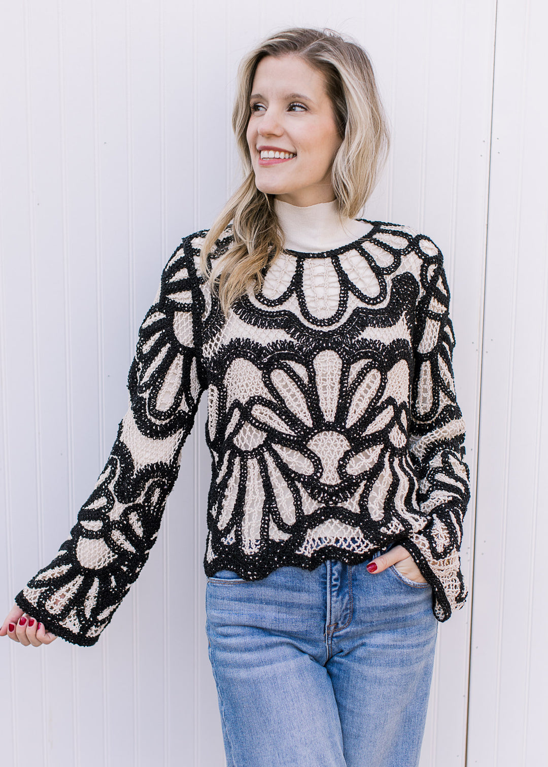 Model wearing a long sleeve cream and black open knit top with a graphic pattern and scallop detail.