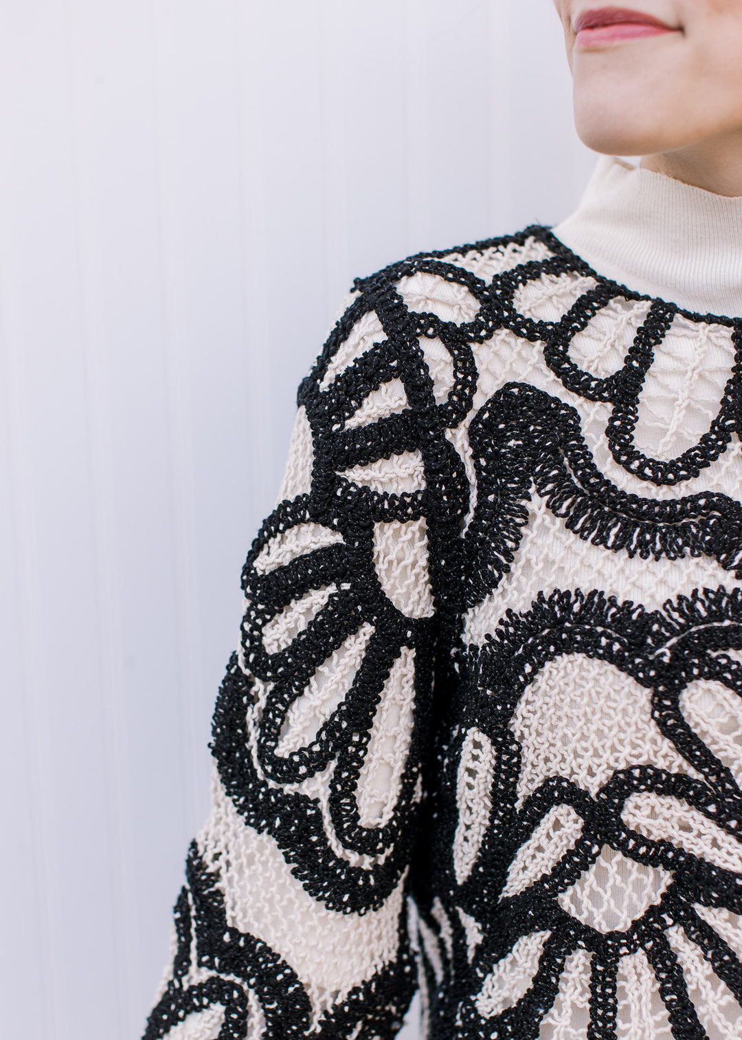 Close up of black graphic design on a cream open knit sweater with long sleeves and round neck. 