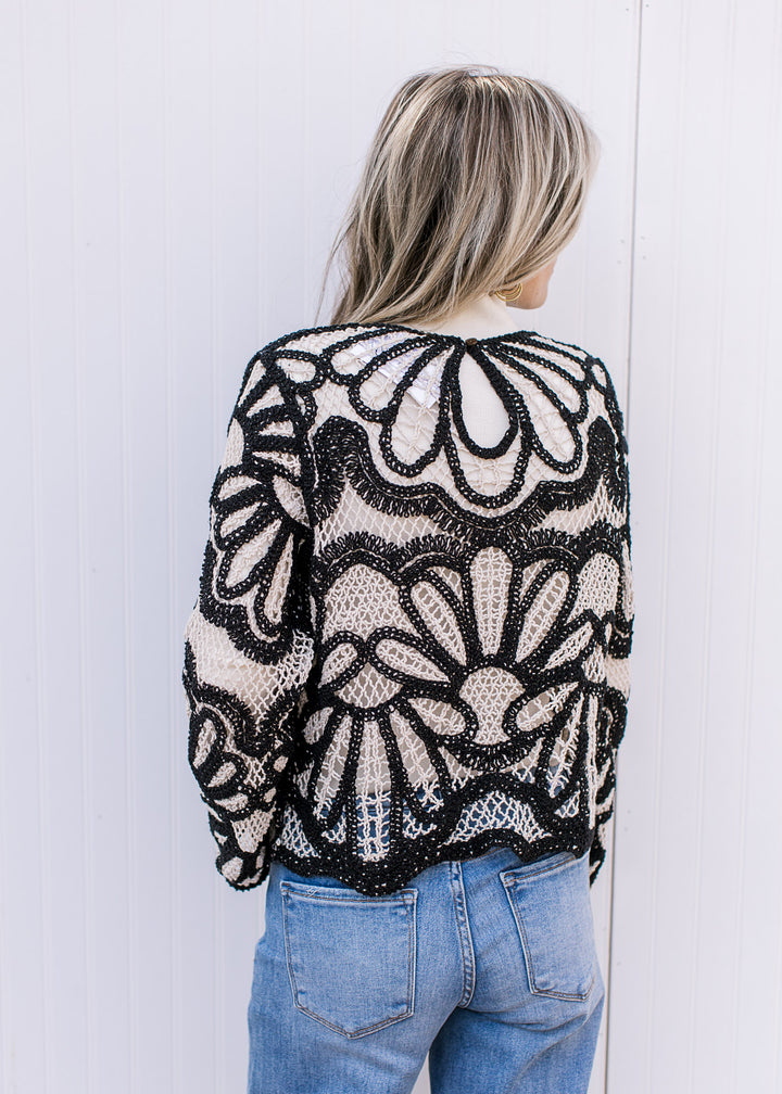 Back view of Model wearing a long sleeve cream and black open knit top with scallop detail at waist.