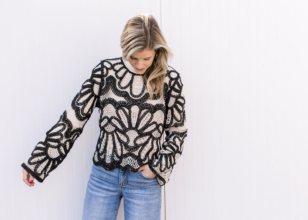 Model wearing a jeans and a long sleeve cream and Black open knit top with scallop detail at waist. 