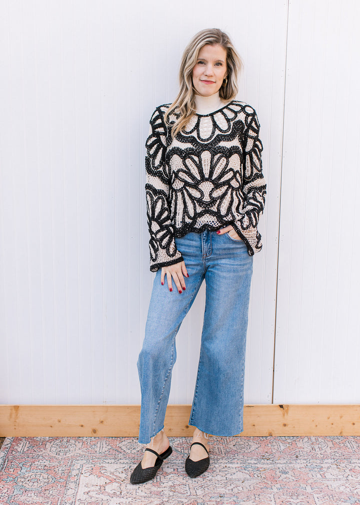 Model wearing flats, jeans and a long sleeve cream and black open knit top with scallop detail. 