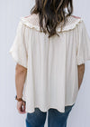 Back view of Model wearing a cream top with rose crochet at neck and bubble short sleeves. 