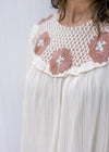 Close up of rose colored crochet at the neck of a cream top with short sleeves. 