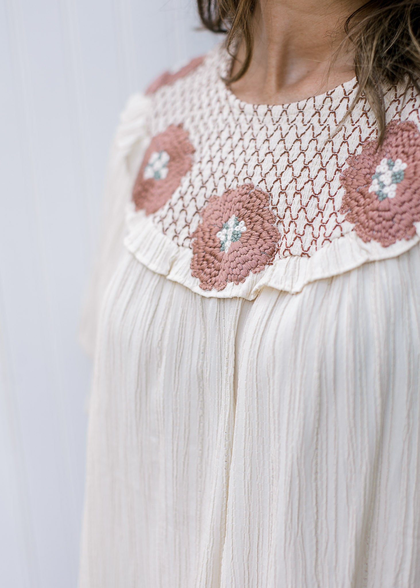 Close up of rose colored crochet at the neck of a cream top with short sleeves. 