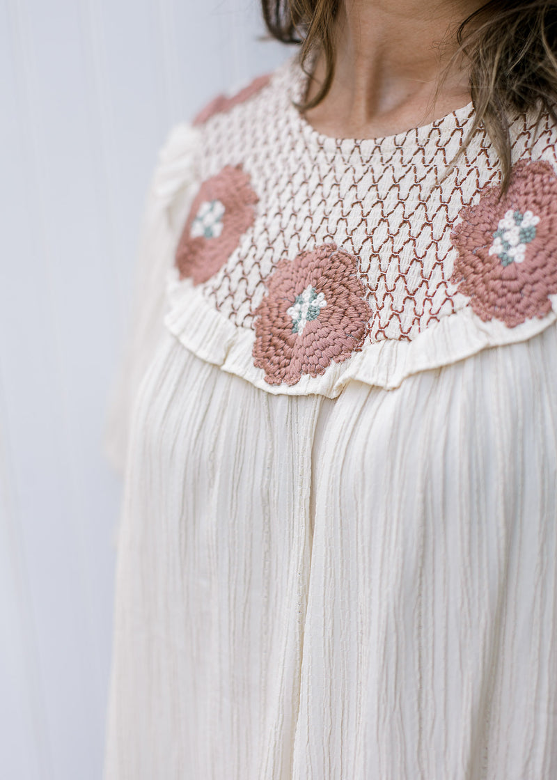Close up of rose colored crochet at the neck of a cream top with short sleeves. 