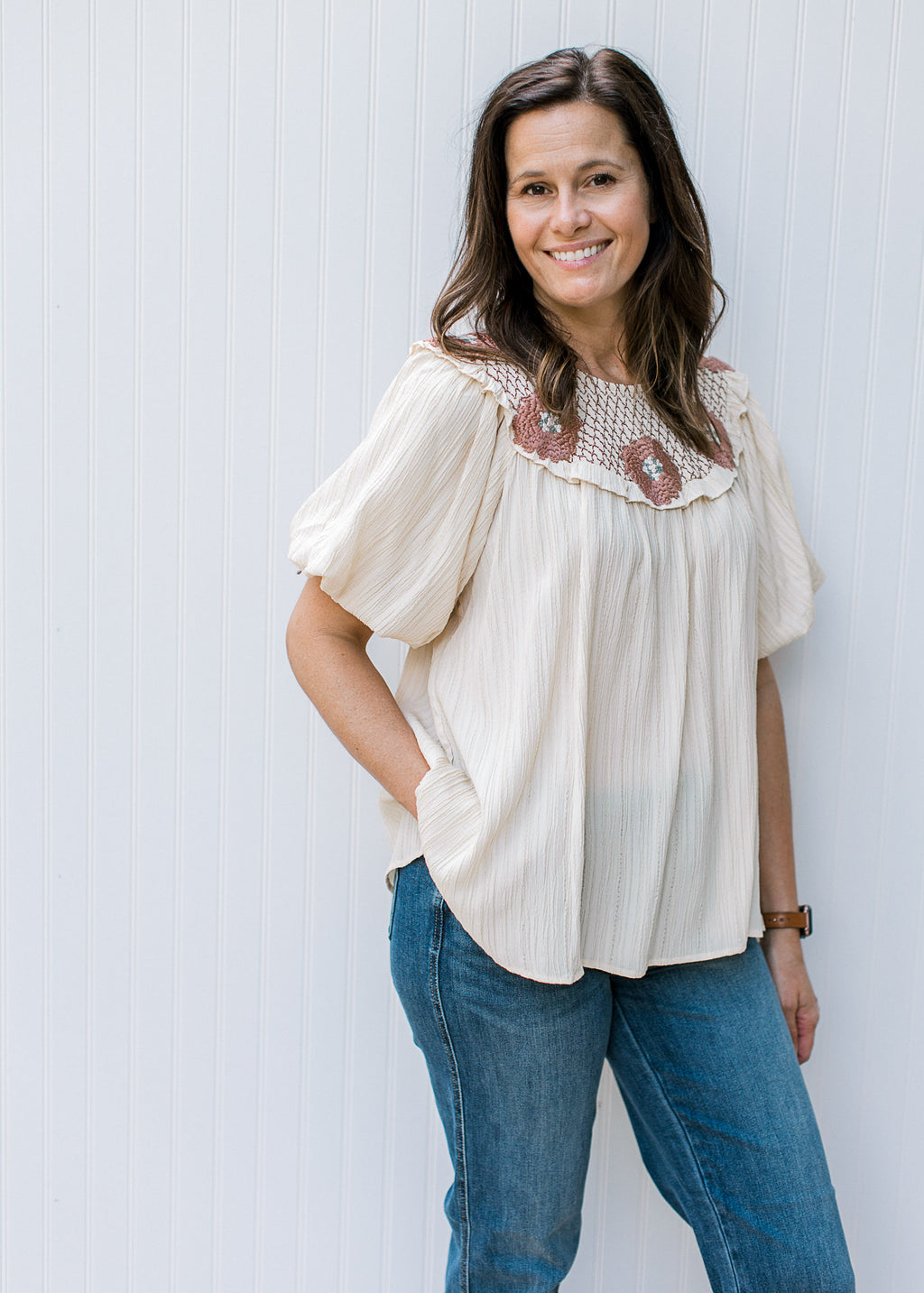 Model wearing a cream top with rose crochet at neck and bubble short sleeves. 