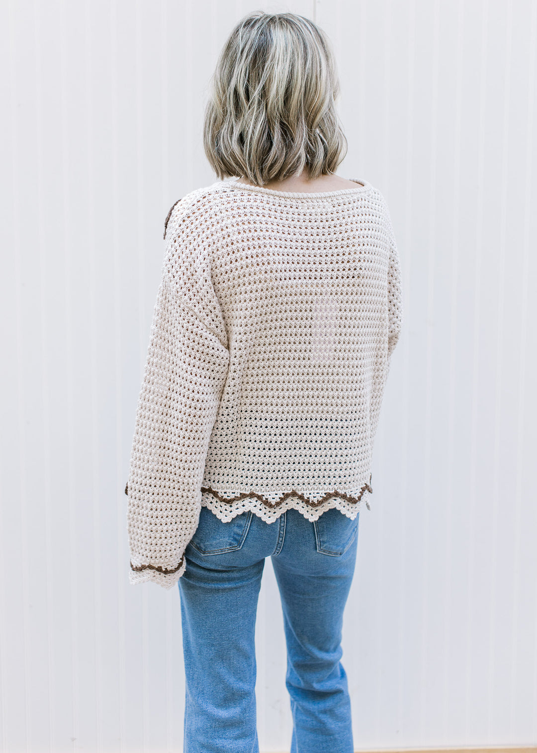 Back view of Model wearing a long sleeve taupe open knit sweater with brown crochet flowers.