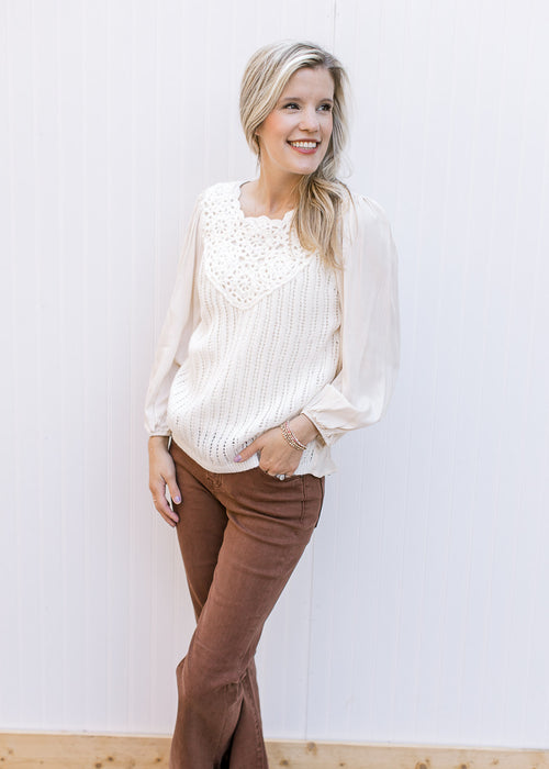 Model wearing a cream top with crochet front, pleated shoulders and slightly sheer 3/4 sleeves.