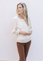 Model wearing a cream top with crochet front, pleated shoulders and 3/4 sleeves with elastic cuff. 