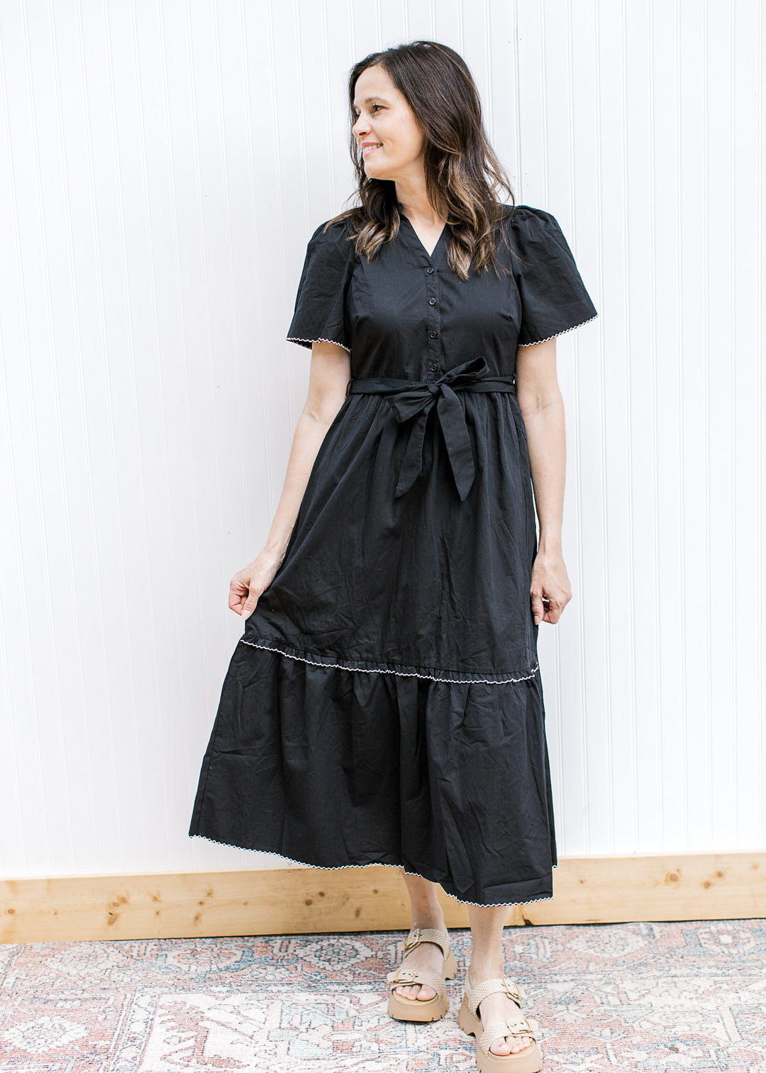 Model wearing a black midi with v-neck and buttons, short sleeves and pleated shoulders. 