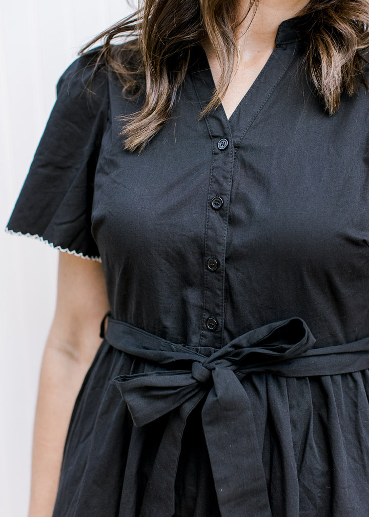 Close up of tie waist and button front with v-neck on a black midi with pleated shoulders. 