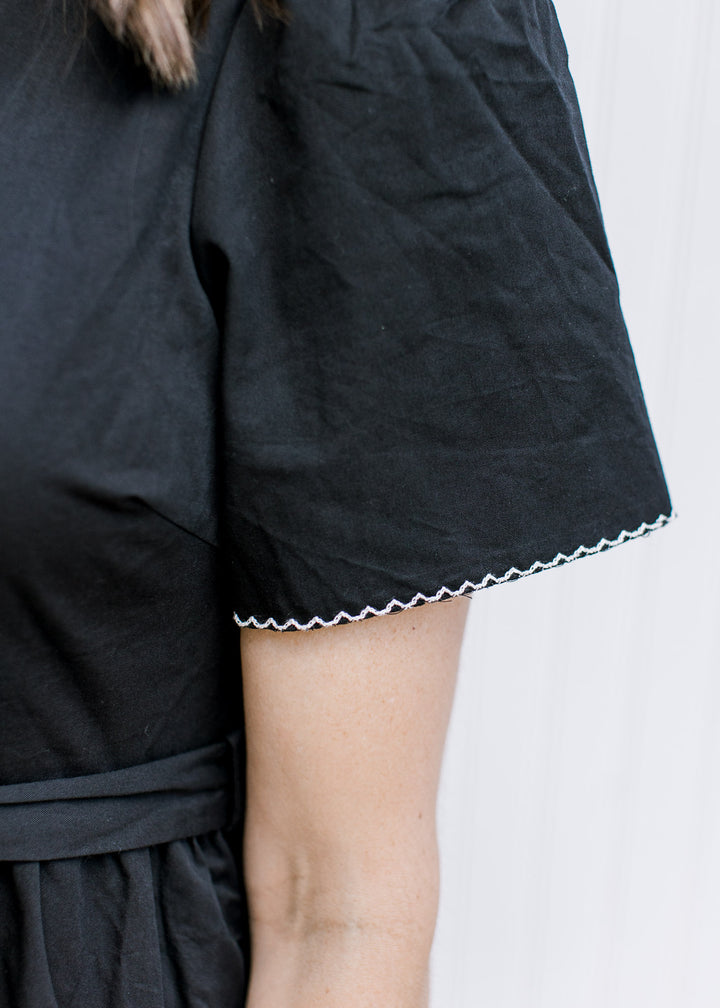 Close up of white trim on the short sleeve of a black midi with a tie at the waist. 