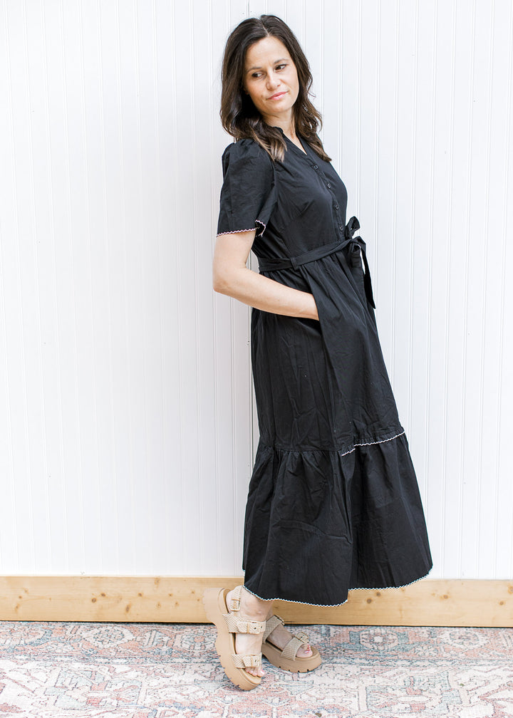 Model wearing a black midi with white trim, pockets, short sleeves and a tie waist. 