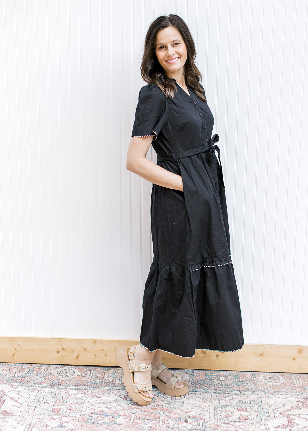 Model wearing wedges and a black midi with white trim, pockets, short sleeves and a tie waist. 