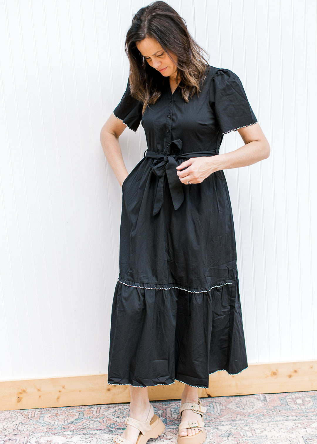 Model wearing a black midi with white trim at short sleeve and tiers, pockets and a tie waist. 