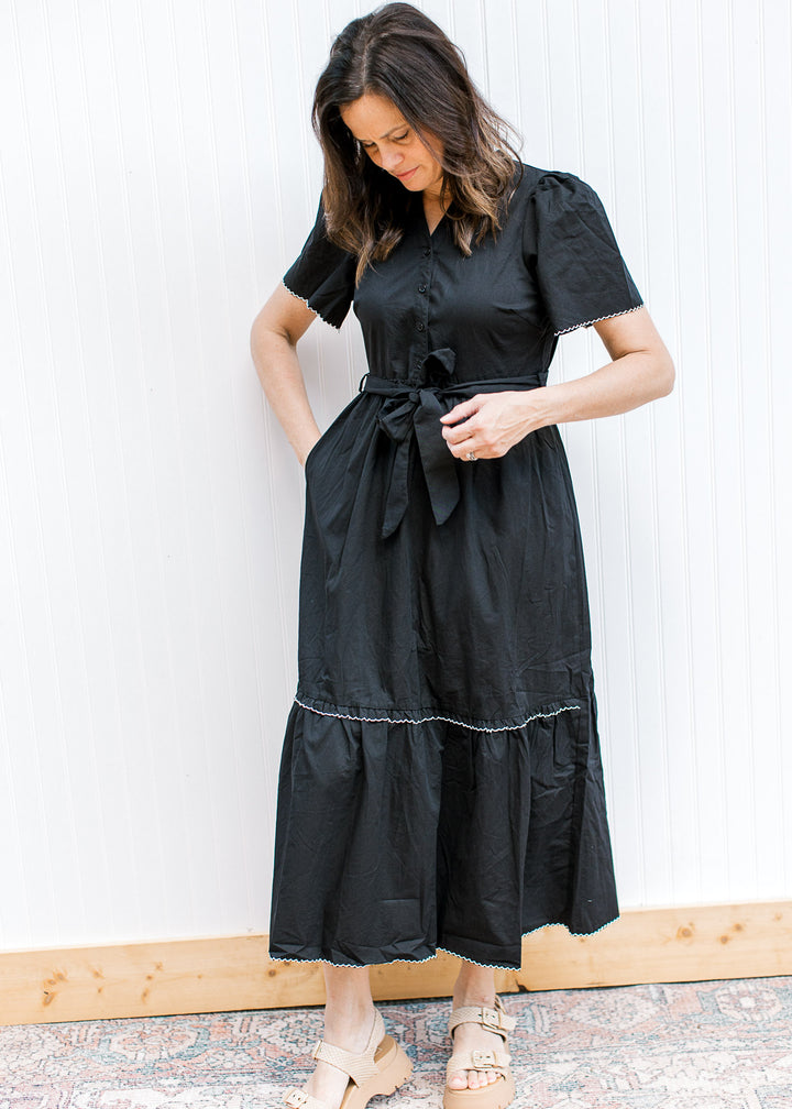 Model wearing a black midi with white trim at short sleeve and tiers, pockets and a tie waist. 