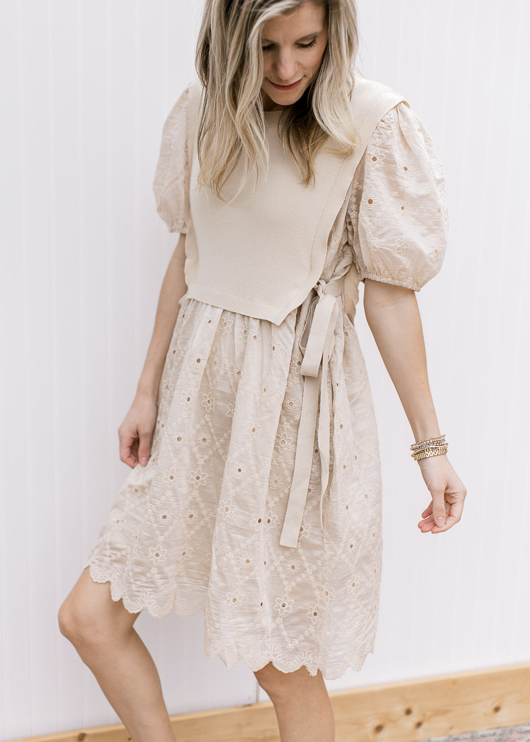 Model wearing a pale coffee, cut lace dress with sweater vest with side ties and short sleeves.