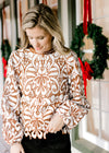 Model wearing a cream top with reddish-brown accents, cut lacework over ivory and long sleeves. 