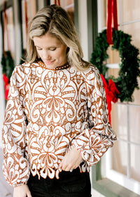 Model wearing a cream top with reddish-brown accents, cut lacework over ivory and long sleeves. 